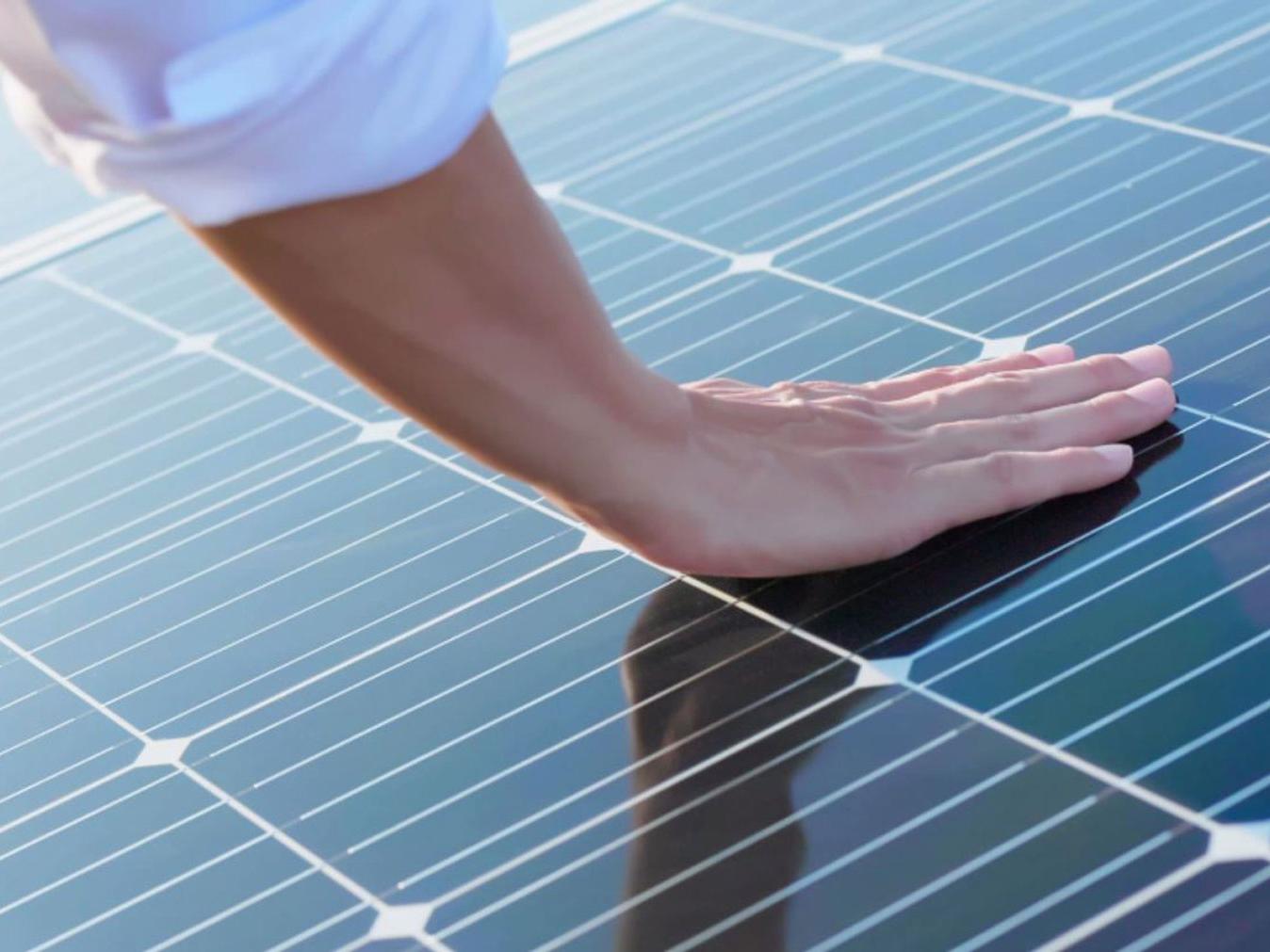 Uma mão encostando em módulos fotovoltaicos. 