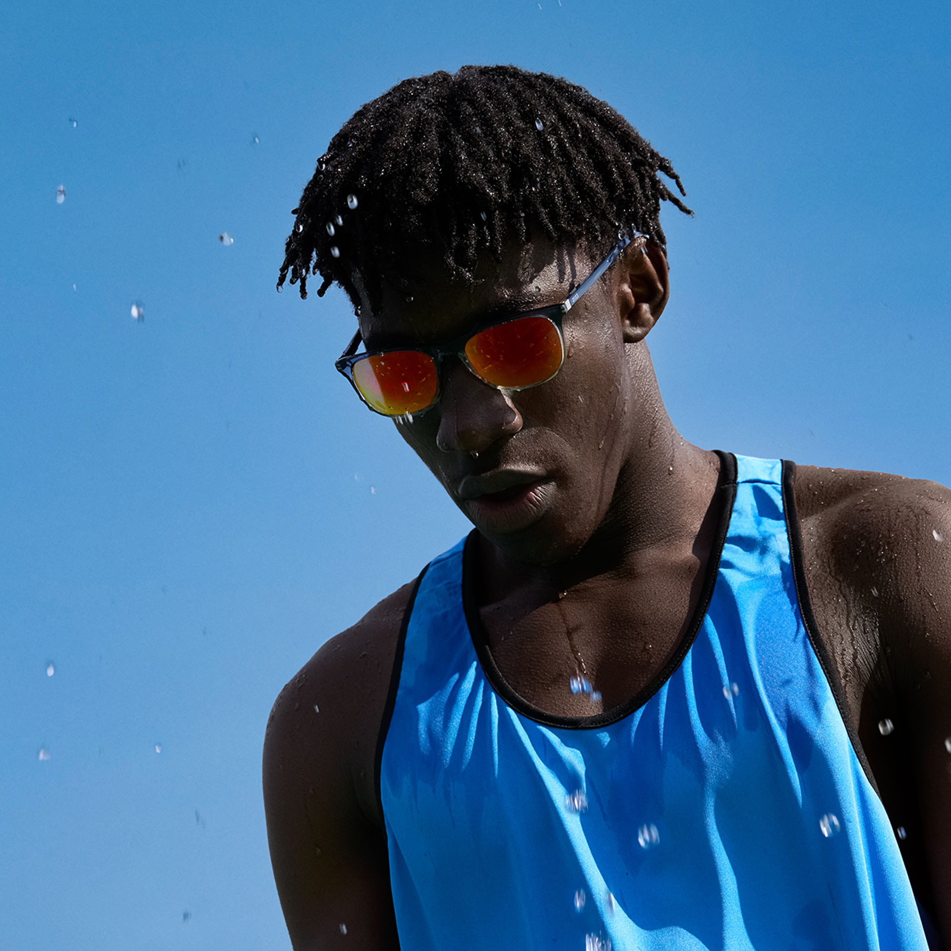 Homem jovem usando uma roupa esportiva e lentes para óculos de sol ZEISS Performance em um tom laranja amarronzado diante do céu azul.