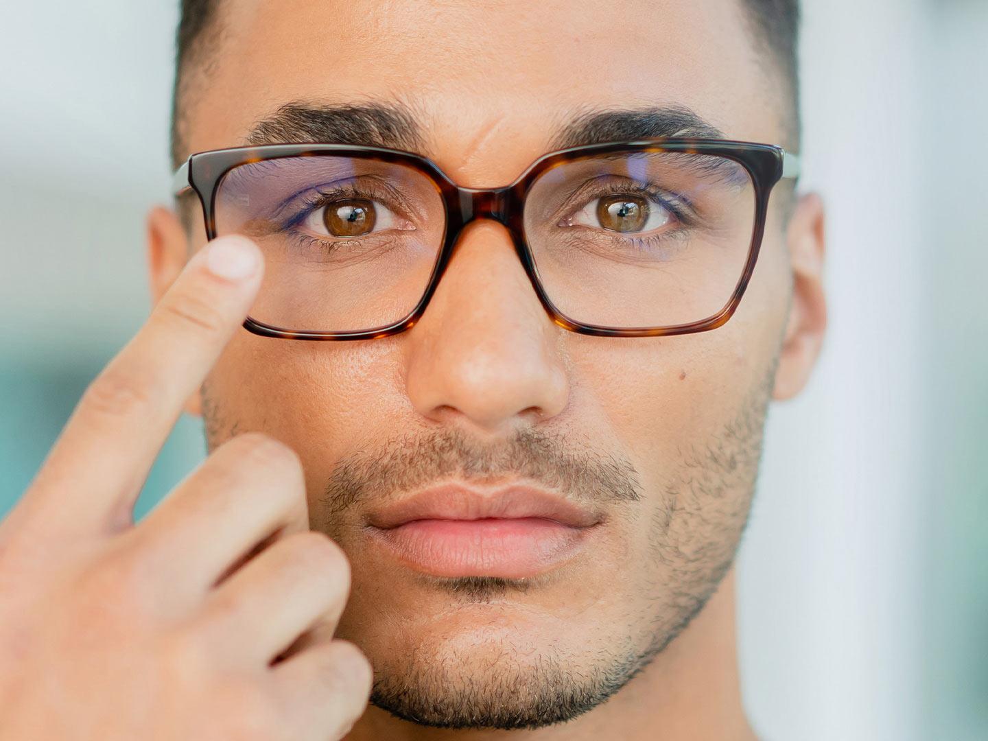 Um homem de óculos tocando a superfície dos óculos
