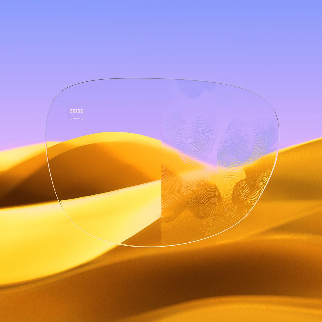 Uma lente de óculos dividida ao meio, com um lado nítido e limpo com ZEISS DuraVision Gold UV e um lado com impressões digitais cobrindo a lente.