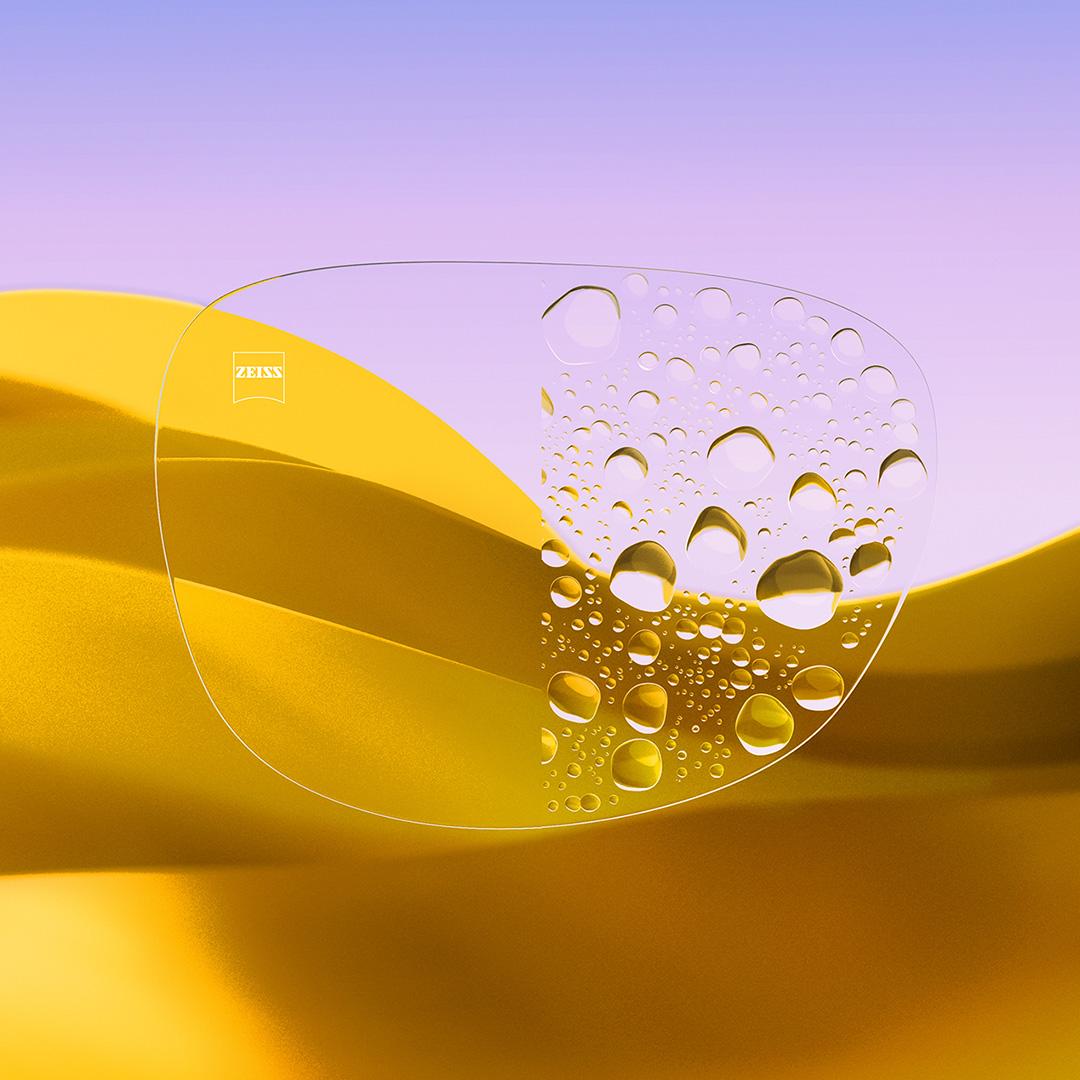 Uma lente de óculos dividida ao meio, com um lado nítido e limpo com ZEISS DuraVision Gold UV e um lado com gotas de água cobrindo a lente.