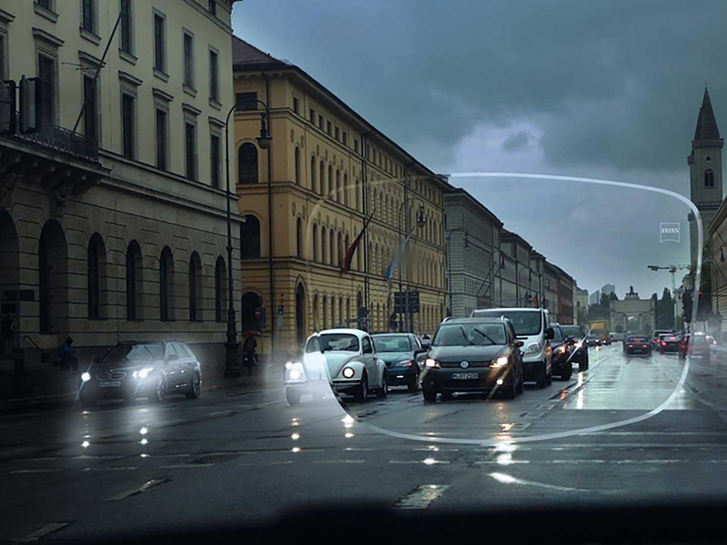 A imagem mostra uma rua com fraca visibilidade e condições de baixa luminosidade. O ponto de visualização é o interior de um carro visto através de uma lente de óculos. 