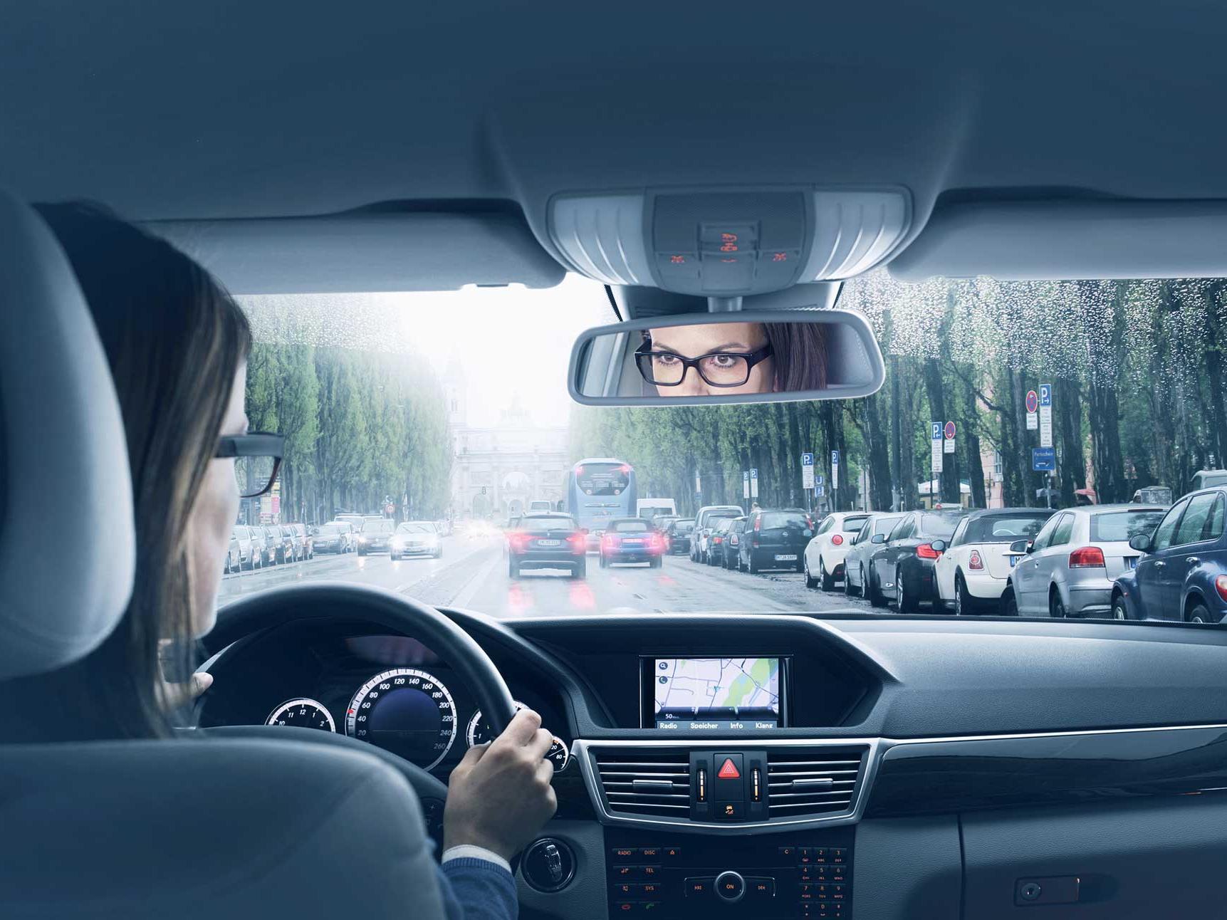 Uma imagem do interior de um carro com uma mulher sentada no banco do motorista. 