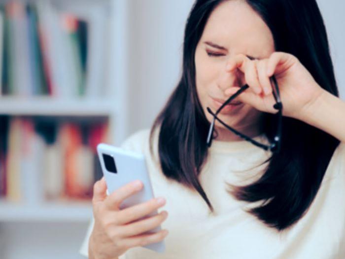 Uma imagem que mostra uma mulher de cerca de 30 anos olhando para o seu telefone enquanto esfrega os olhos.