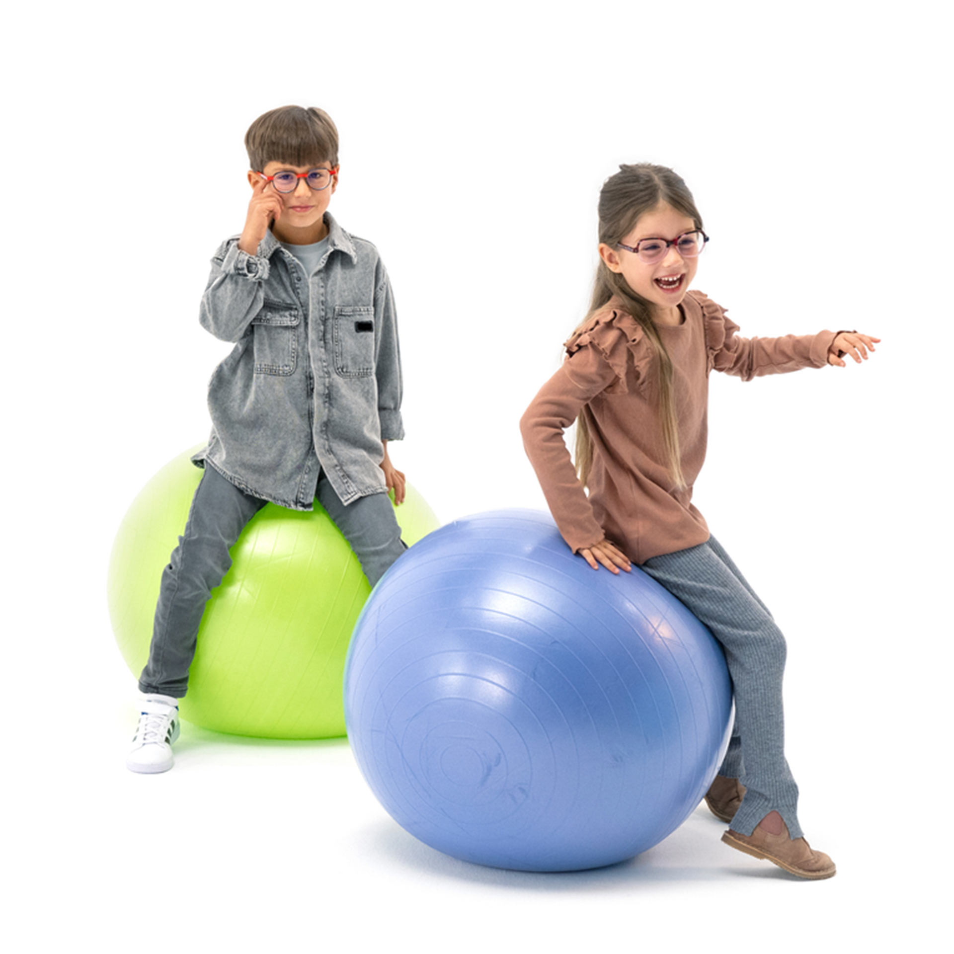 Um menino e uma menina, ambos de óculos, brincam alegremente com bolas de ginástica.