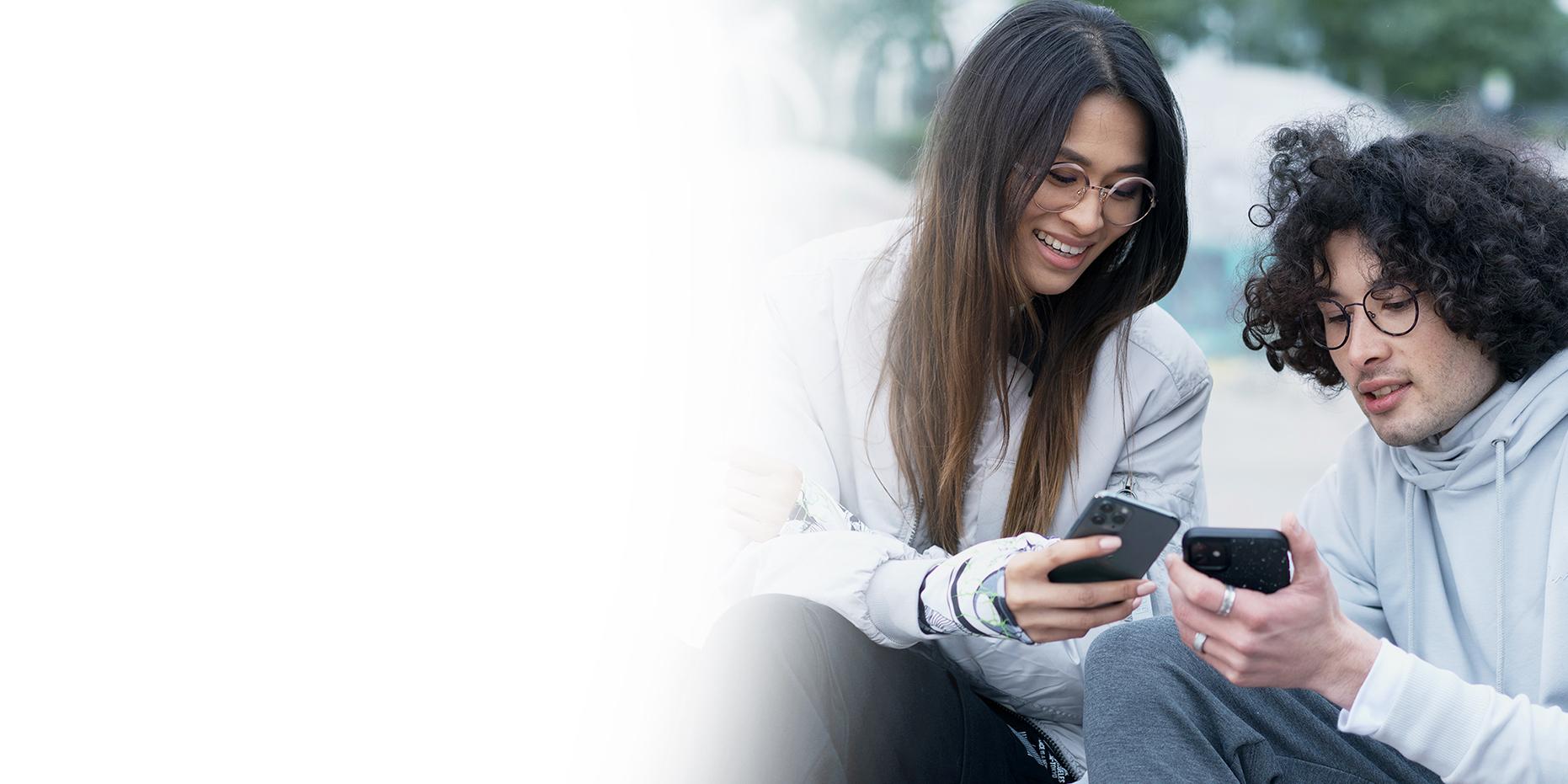 Dois jovens, uma mulher de cabelo castanho comprido sorrindo e um menino de cabelo preto encaracolado com óculos ZEISS SmartLife, ambos olhando para os seus telefones. 