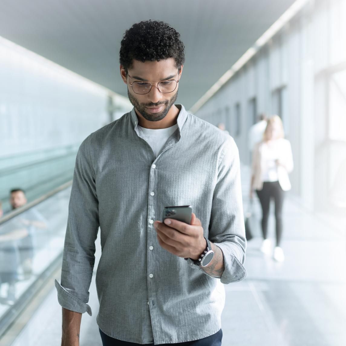 Um jovem com lentes ZEISS SmartLife olhando para o celular enquanto caminha.