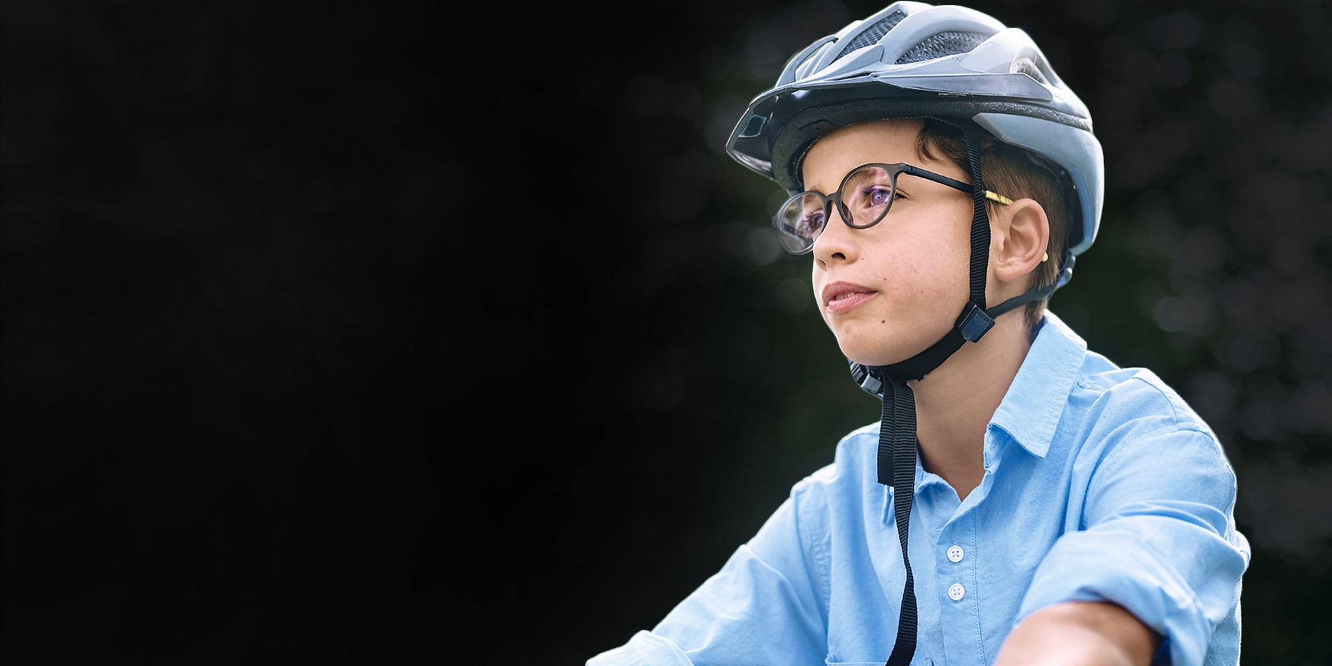 Um menino com óculos e capacete, aparentemente andando de bicicleta.