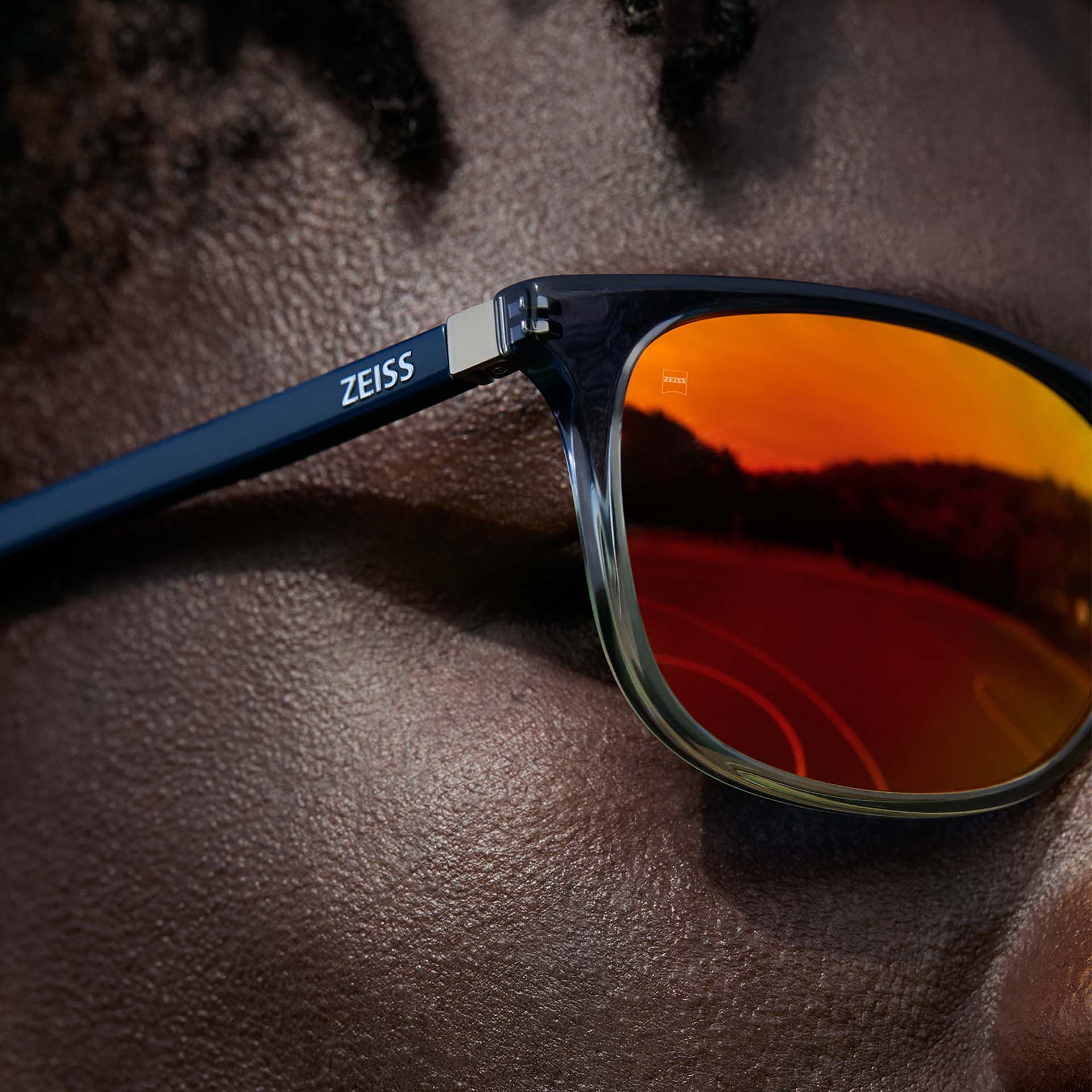 Imagem aproximada de um homem usando óculos ZEISS com tratamento ZEISS DuraVision Mirror UV para óculos de sol na cor laranja.