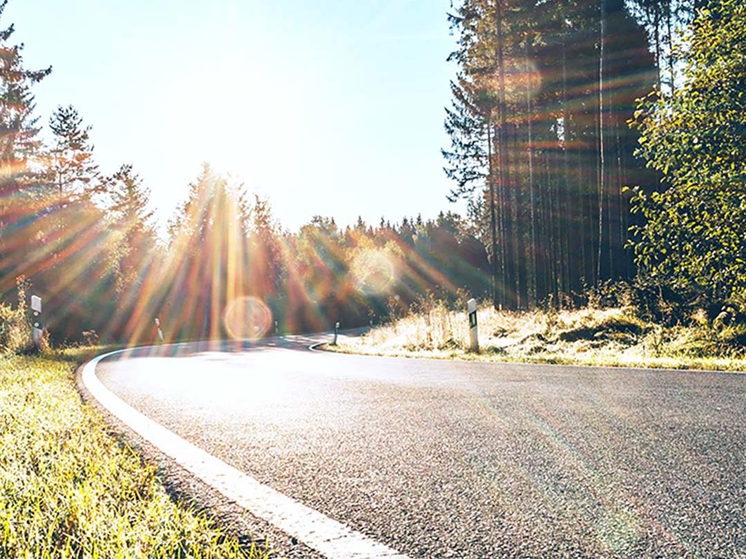 Imagem deslizante em que metade mostra uma estrada em uma área de bosque com luz solar intensa e a outra metade mostra a mesma estrada com ofuscamento reduzido e maior contraste, enfatizando o efeito das lentes polarizadas para óculos de sol.