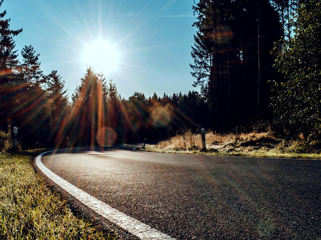 Imagem deslizante em que metade mostra uma estrada em uma área de bosque com luz solar intensa e a outra metade mostra a mesma estrada com ofuscamento reduzido e maior contraste, enfatizando o efeito das lentes polarizadas para óculos de sol.