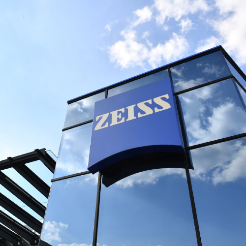 Imagem de um prédio moderno de vidro com um grande logo ZEISS. 