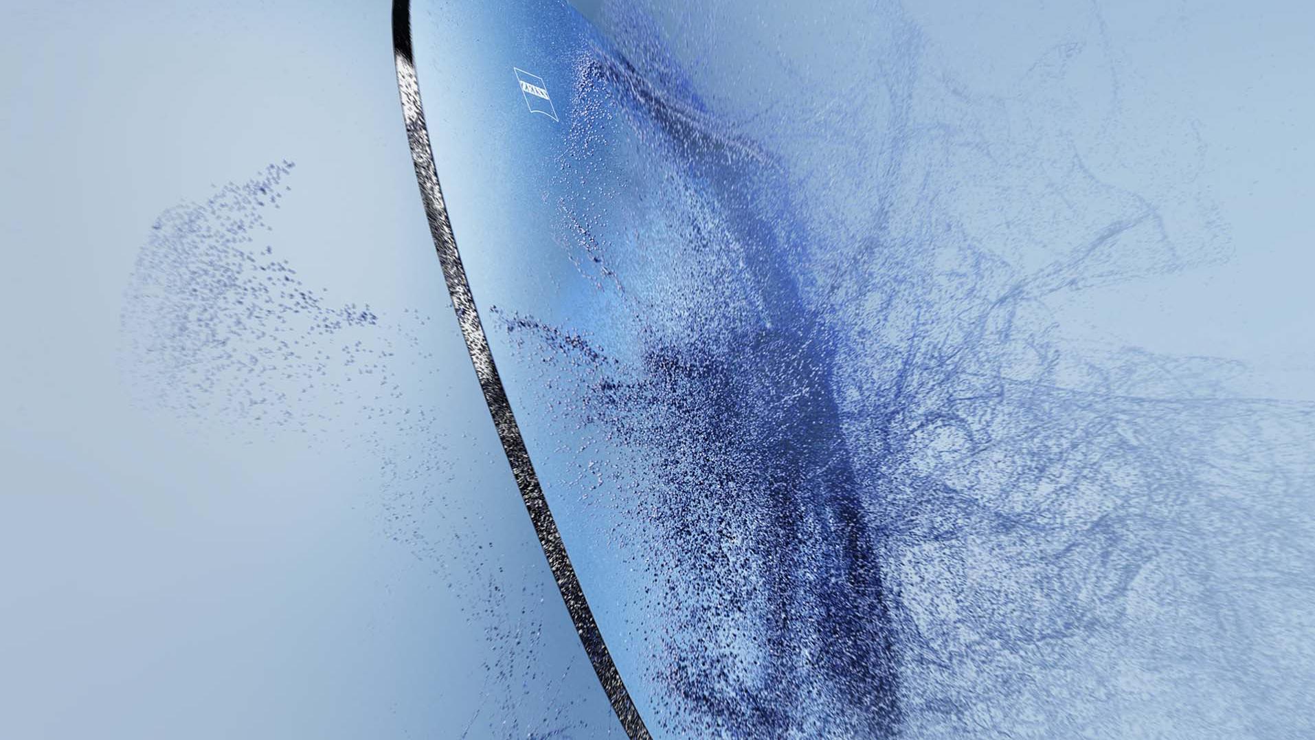Uma lente de óculos com o logotipo da Zeiss colide com areia.