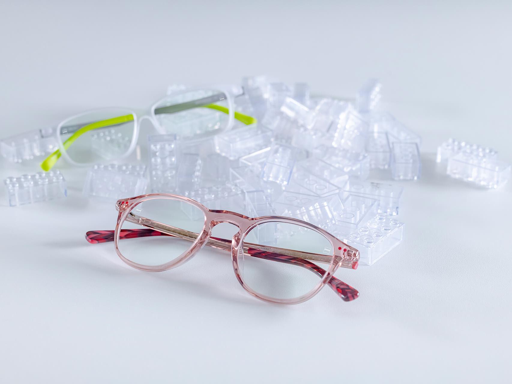 Dois pares de óculos infantis com lentes ZEISS e tratamento DuraVision® para crianças. Os óculos estão posicionados entre blocos de brinquedo transparentes.