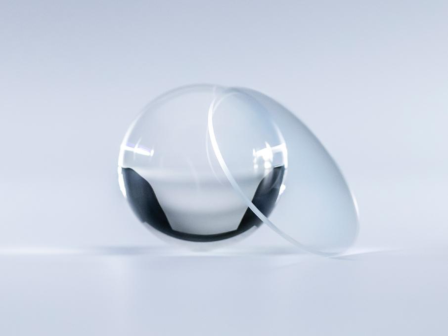 Uma lente com revestimento ZEISS Platinum totalmente transparente e sem reflexos em comparação com uma bola de vidro ao seu lado.