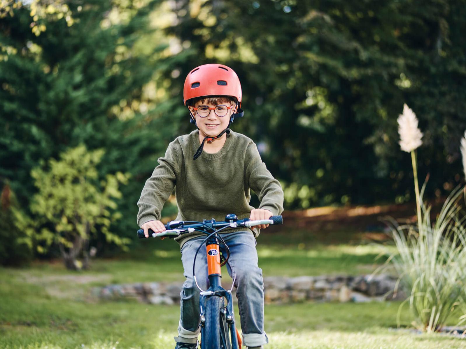 Menino pequeno usando lentes ZEISS para gerenciamento de miopia enquanto anda de bicicleta.