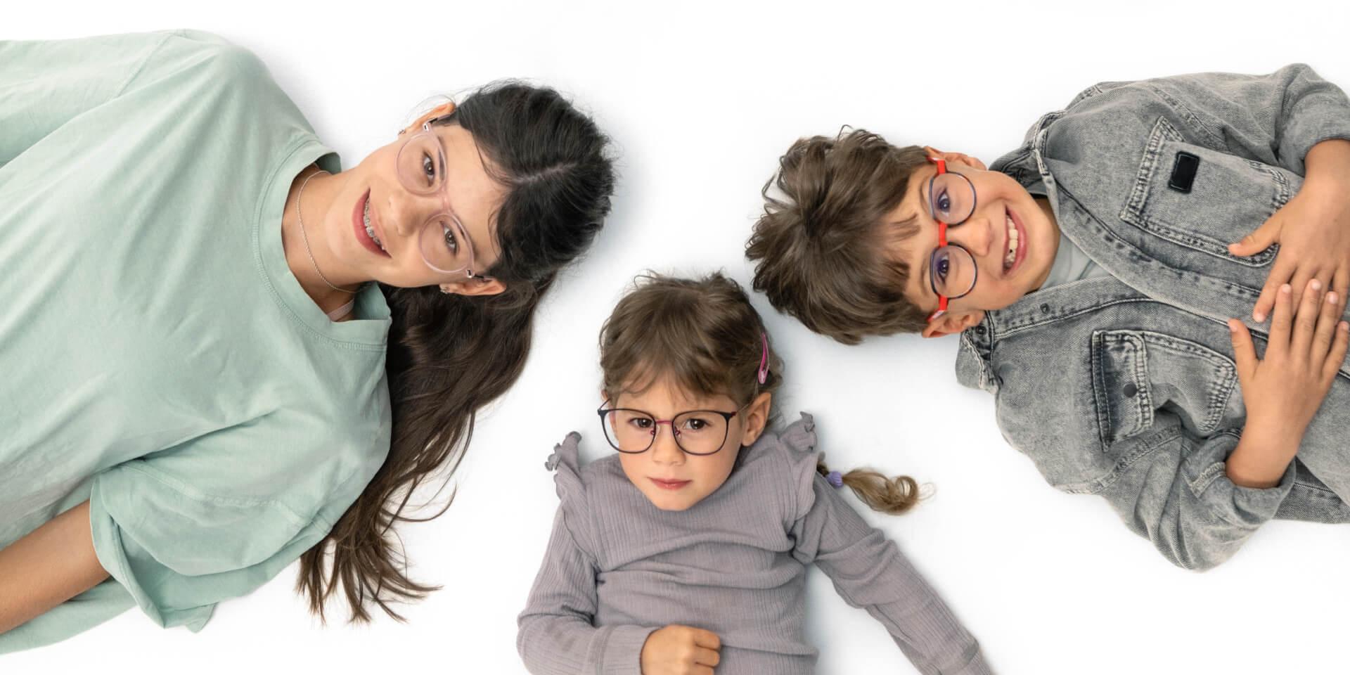 Um adolescente e duas crianças mais novas deitados no chão usando lentes ZEISS Myopia.