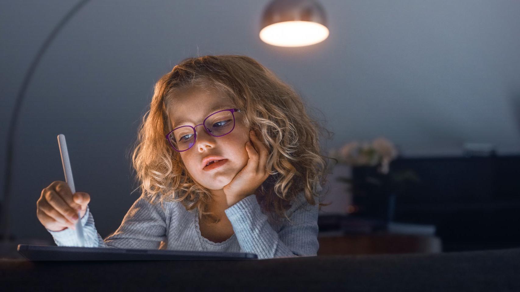 Menina olhando para um tablet em uma sala escura.