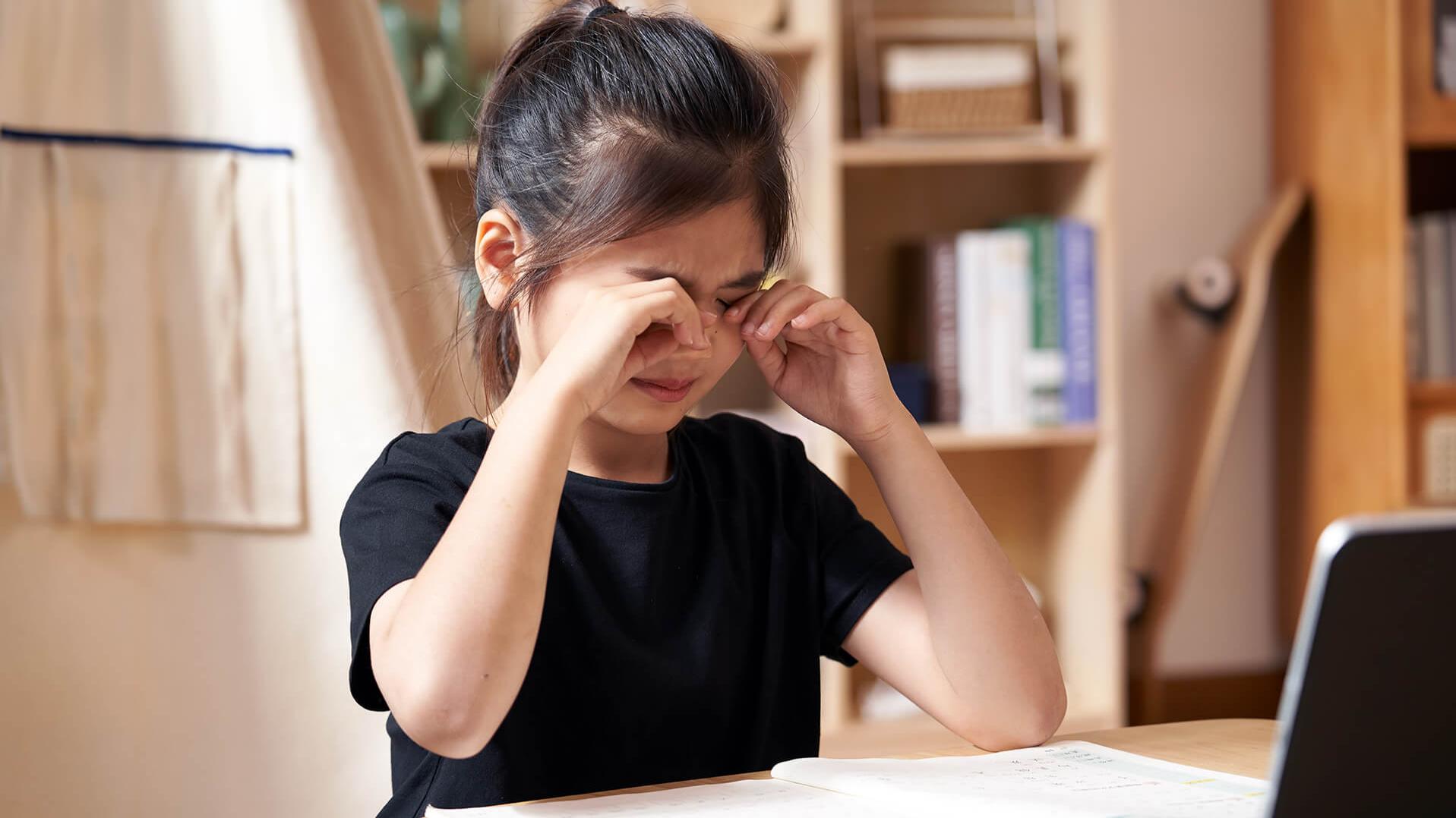 Menina esfregando os olhos enquanto faz um trabalho escolar.