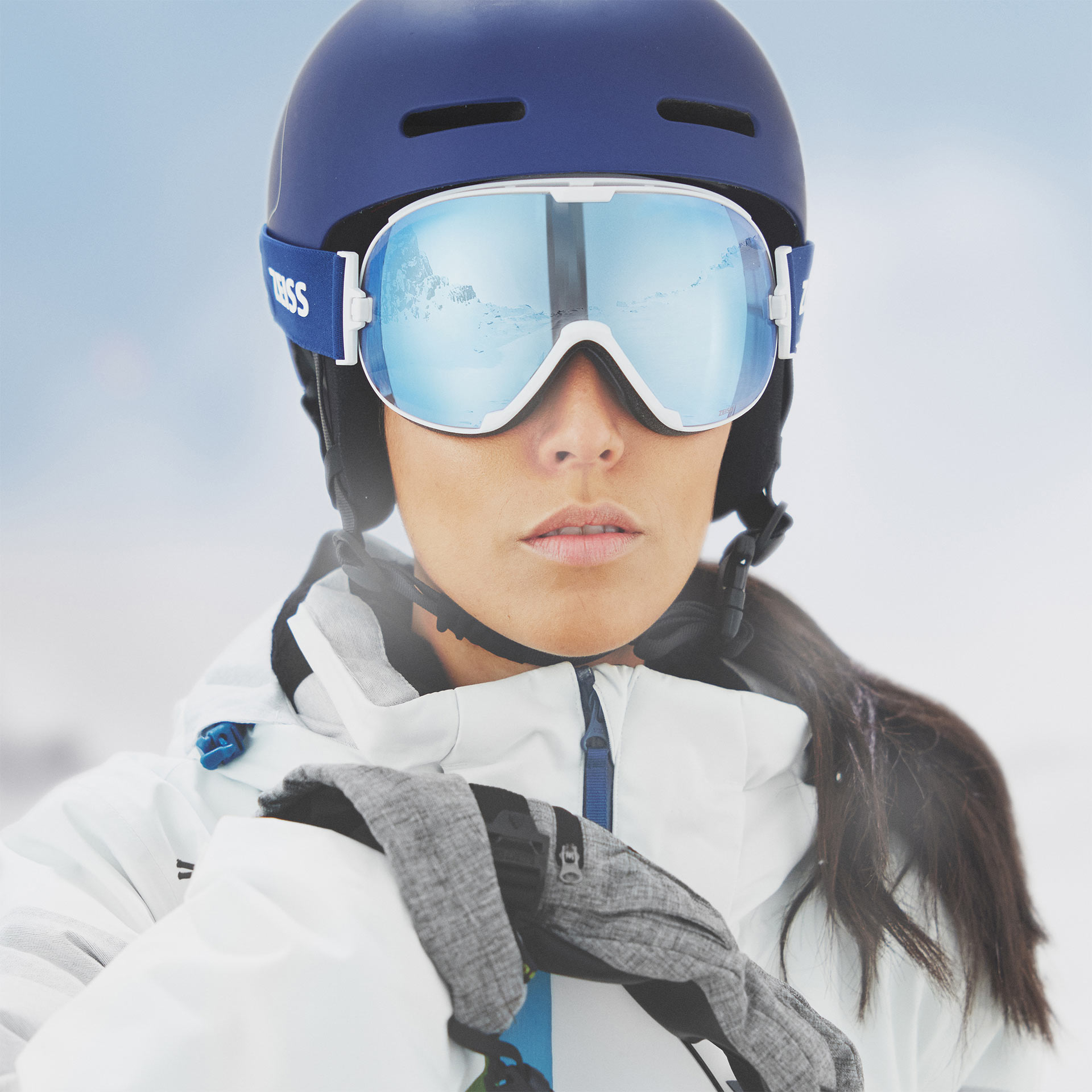 A woman wears a blue helmet with blue mirrored ZEISS ski goggles.