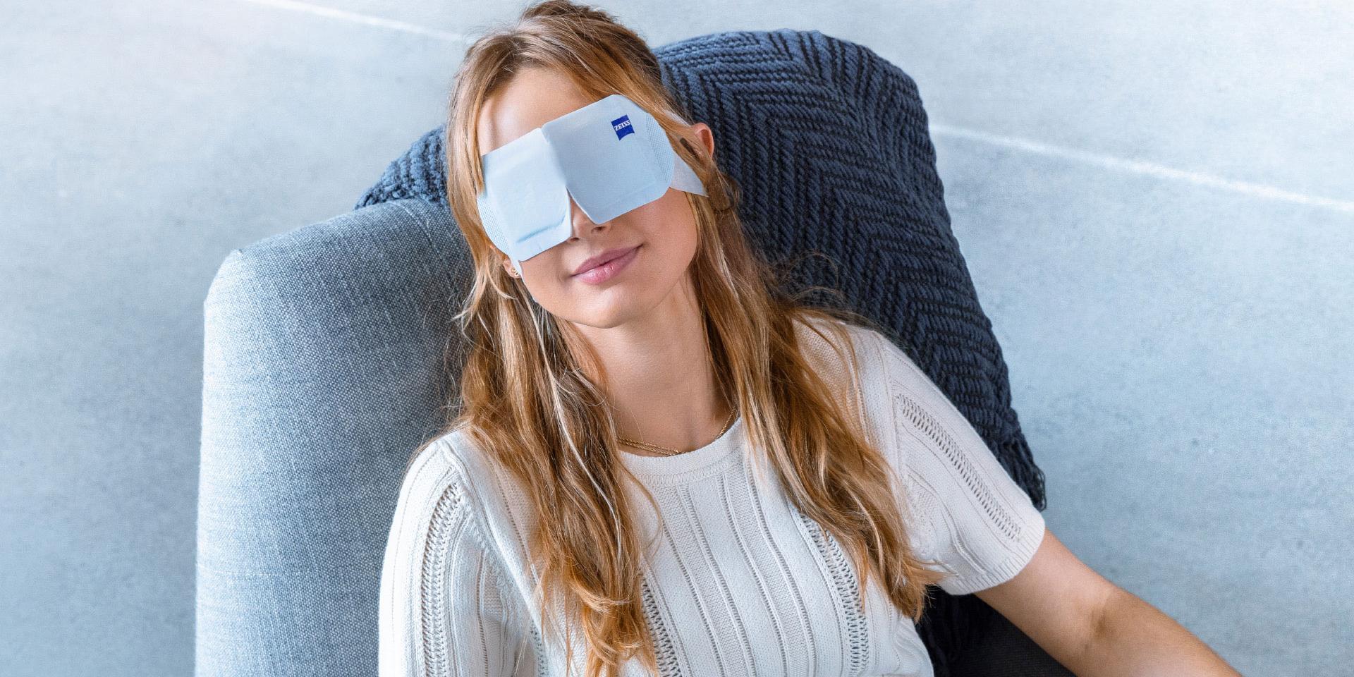 Mulher usando a ZEISS Warm Eye Mask enquanto relaxa em uma cadeira.