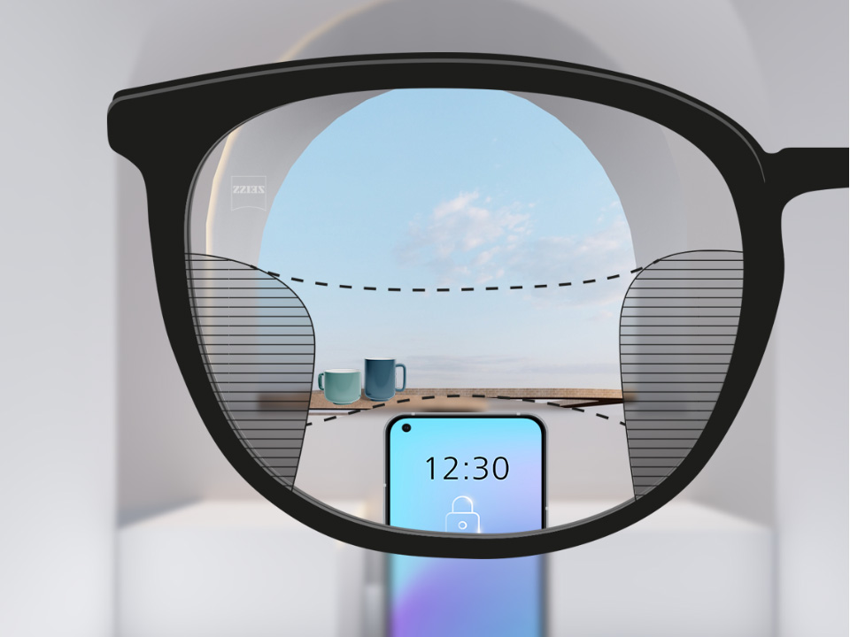 Imagem mostrando as lentes ZEISS Progressive SmartLife com um smartphone e xícaras em segundo plano enquanto a lente está totalmente transparente, mas com linhas finas borradas à direita e à esquerda.