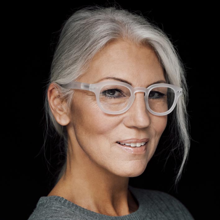 Mulher com cabelos grisalhos usando uma armação branca com lentes progressivas ZEISS SmartLife. Digitalização de rosto geométrico mostrando a anatomia facial e as medidas da armação.
