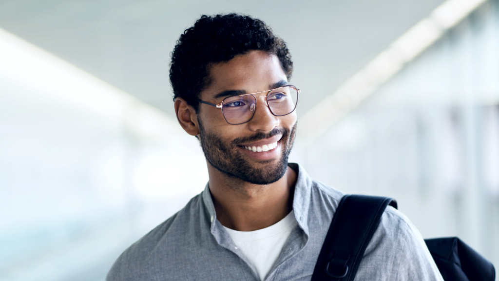 Um jovem sorrindo com uma mochila no ombro, usando óculos com lentes ZEISS Digital SmartLife e olhando para o lado.